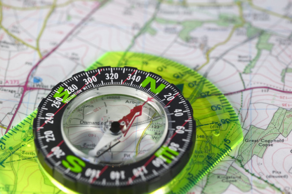 Translucent green compass on top of a map with the red magnetic needle pointing toward the north 